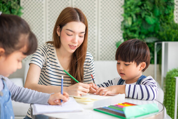 happy loving family. pretty young mother reading a book and drawing to her daughter and son.Mother teach Asian preschool student do homework by reawing by a color.