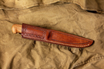 A knife with a fixed blade in a leather sheath with a pattern on a brown canvas. Traditional...