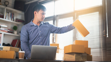 Asian male business owner using computer laptop checking parcel boxes. Asian entrepreneur seller using computer laptop for preparing retail package postal shipping order at home.