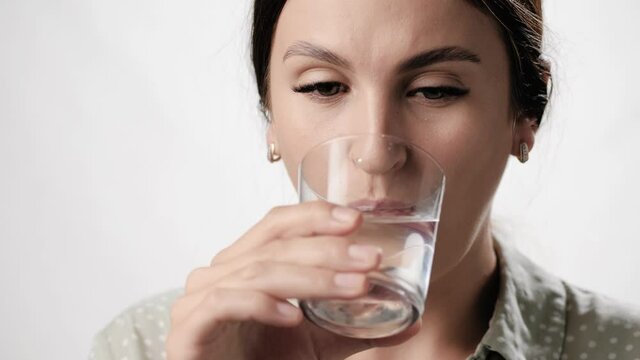 Sensitive teeth. Woman on white background drinks water from glass and has toothache due to sensitivity of her teeth. Close-up and slow motion