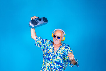 Senior man dancing clubbing with boombox and wireless headphones having fun on holiday