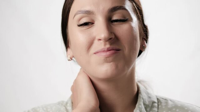 Neck pain relief. Happy woman on white background touches her neck with her hand and smiling looks at camera. Close-up and slow motion