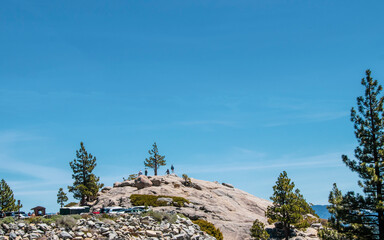 Tourists on rock hill above parking area  looking out over Lake Taho with pinke trees around and...