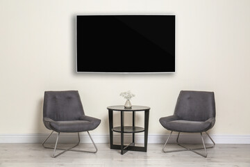 Modern wide screen TV on white wall in room with stylish furniture