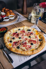 Pizza with prosciutto and olives with wine in restaurant