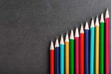 Pencils of different colors in a row on a black textured background.