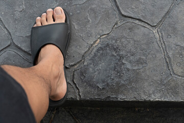 focus on men's feet wearing black sandals. Man wearing black shorts walks up the stairs. Concrete floor painted with black stone pattern.