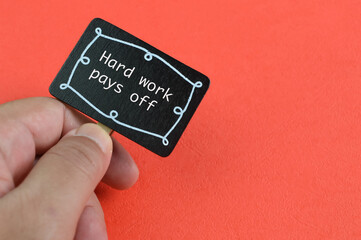 Hand holding wooden board written with text HARD WORK PAYS OFF