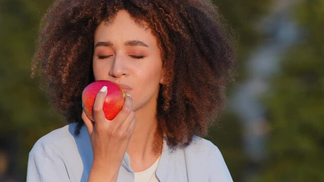 Beautiful young happy black african american girl with pleasure eat delicious red apple healthy vegetarian food weight control. Smiling Mixed race afro woman female eating fruit vitamin good habit
