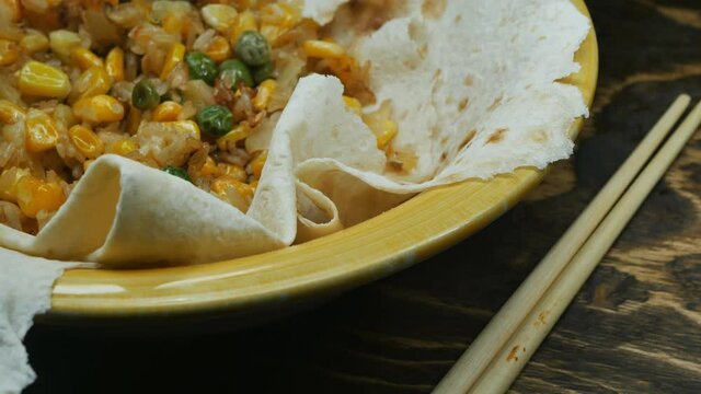 close-up Asian and Oriental dish roasted corn, green peas, rice and pineapple pieces in pita bread in a yellow bowl on a brown wooden tray and hashi chopsticks, rotate slowly.