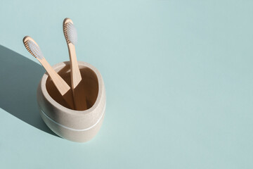 Two eco friendly bamboo wooden toothbrushes in a glass on a blue background. Hard light.