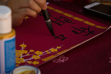 manos escribiendo letras chinas con tinta negra sobre superficie roja