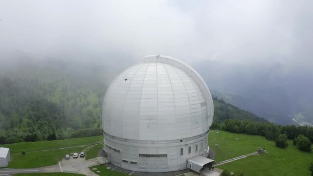 Nizhny Arkhyz, Russia - June 26, 2021: Aerial view of Astrophysical observatory of Russian Academy of Sciences. Drone goes up through moving clouds above BTA tower. Astronomy Caucasus scenic landscape