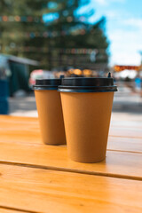 Two paper cups with a lid of coffee take-away in street cafe. Wooden table and place for text. 