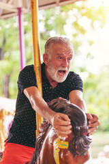 Smiling senior man on horse carousel ride at the amusement theme park, male senior tourist, elderly...