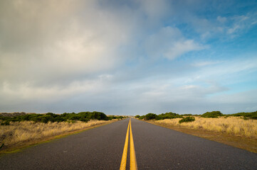 Converging lines country road with dunes and cloudy sky