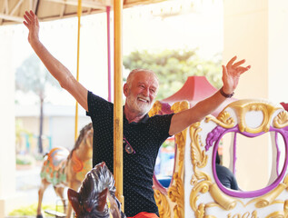 Smiling senior man on horse carousel ride at the amusement theme park, male senior tourist, elderly man having fun, relaxing at the theme park. people, tourist and holiday concept © amorn