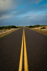 Converging lines country road with dunes and cloudy sky