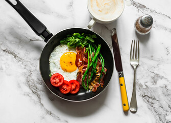 Delicious breakfast in a frying pan - fried egg, bacon, asparagus, tomatoes on a light background, top view