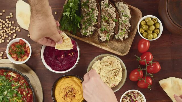 Israeli cuisine. Shakshuka in pan decorated with parsley, forshmak and hummus on table, eating pita with sauces. National Jewish dishes top view. Eggs fried in tomato sauce, middle eastern culture.