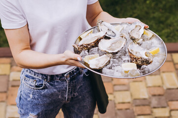 Fresh oysters on white plate with lemon and ice on the waiter hands