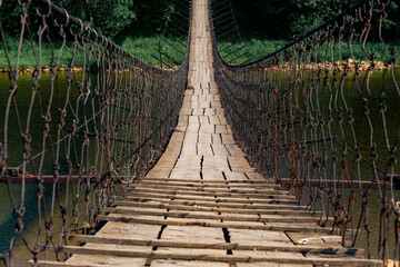 old rural suspension bridge over the river goes into perspective