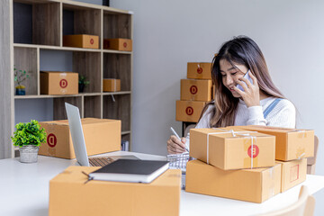 A woman talks on the phone and uses a laptop to confirm orders from customers on the website, packs the goods in parcels and sends them through a private courier company. Online shopping concept.