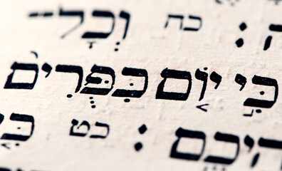 Closeup of hebrew words Yom Kippur in Torah page that translate in english as Day of Atonement, holiest day of the year in Judaism. Selective focus.