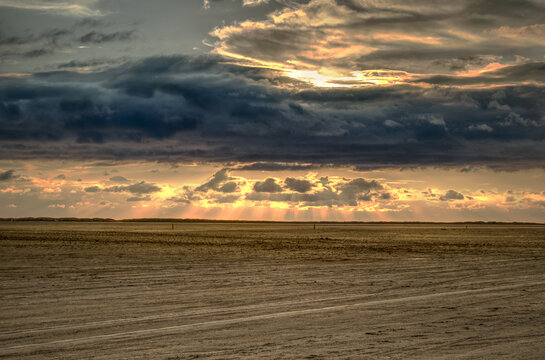 Orange light  breaks through the clouds at sunset at the beach while it is ebb