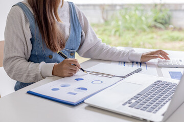 Woman holding a pen pointing to documents on a desk, she is a financial scholar, she is checking...