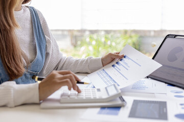 Woman holding a document and pressing a white calculator on her desk, an auditor is reviewing company bookkeeping data to verify validity and fraud, accounting manipulation. Audit concept.