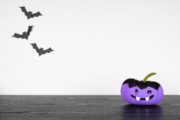 Painted Halloween pumpkin vampire on a black shelf against a white wall with bats. Copy space.