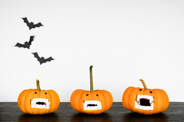 Fun Halloween pumpkins with vampire teeth on a black shelf against a white wall with bats. Copy...
