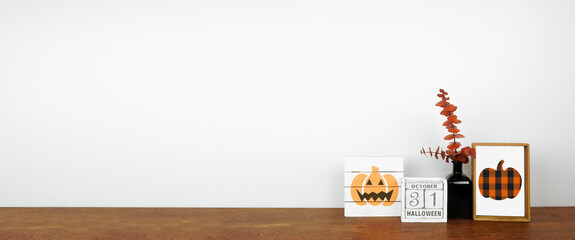 Halloween decor on a wood shelf. Shabby chic wood signs, calendar and orange branches against a white wall banner. Copy space.