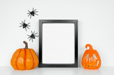 Halloween mock up. Black frame with pumpkin and jack o lantern decor on a white shelf. Portrait...