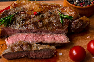 Grilled medium rare meat piece of ribeye beef meat on wooden cutting board on a wooden table stacked tomatoes garnished with hot peppers, peppercorns, , himalayan salt. Fresh food. BBQ. Macro