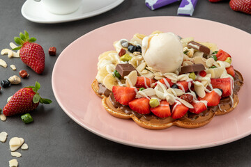 Heart waffle with banana and strawberry with gummy candy and ice cream on it.