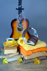guitar, headphones on a stack of yellow, orange clothes, books, autumn leaves, cup of hot tea, coffee, seasonal concept, cozy autumn mood