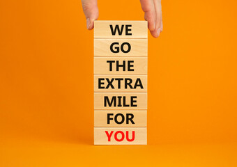 Go the extra mile symbol. Wooden blocks with words 'We go the extra mile for you'. Businessman hand. Beautiful orange background. Business and go the extra mile concept. Copy space. - obrazy, fototapety, plakaty