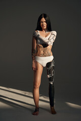Full length view of the tattooed female with cyborg pattern on her body posing at the studio on dark background. People and robot concept - obrazy, fototapety, plakaty