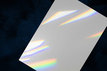 Close up of empty white vertical rectangle a4 poster or business card mockup, lying diagonally with overlay of rainbow light refraction caustic effect and shadow on dark blue concrete background