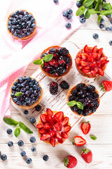 Tasty tartlets with berries on wooden table, top view.