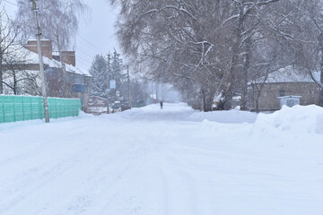Winter. Snowing. Snowdrifts lie on a rural street, a pedestrian is walking.