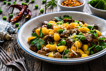 Gnocchi with fried white mushrooms, green peas, parmesan and parsley on wooden table
