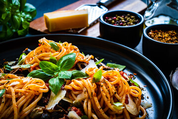 Pasta puttanesca with tomato sauce, anchovies, chilli, capers and olives on wooden table
