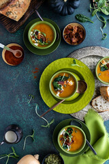 Top down vertical view of bowls of butternut squash soup surrounded by topping ingredients, ready for eating.