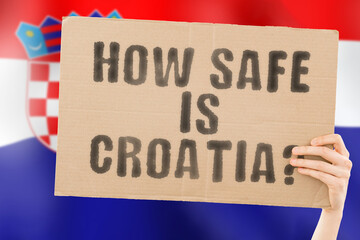 The question " How safe is Croatia ? " on a banner in men's hand with blurred Croatian flag on the background. Safety. Street. Outdoor. Dangerous. Security. Attack. Criminal. Criminality
