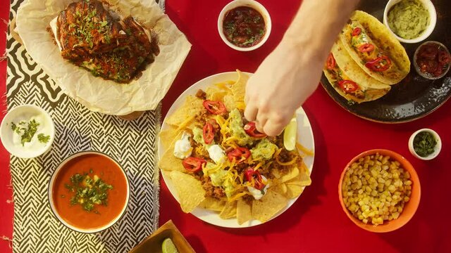 Mexican food, traditional tex mex cuisine. Squeezing lime juice on corn nachos served with meat and vegetables. Tomato soup with cilantro, guacamole. Setting the table with American dishes top view.