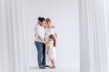 Young modern family have fun together in white loft interior. Mother pregnant, father holds daughter