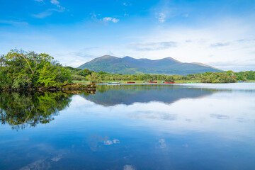 Scenic view across Lake Ross to boats on other-side and distant mountains with light and shadow from sun and clouds, Killarney National Park